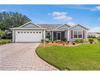 Charming single-story home featuring a manicured lawn, brick driveway, and attached two-car garage at 8980 Se 176Th Limerick Ln, The Villages, FL 32162