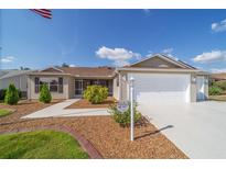 Inviting home with tan siding, manicured lawn, two-car garage, and mature landscaping at 997 Nash Loop, The Villages, FL 32162