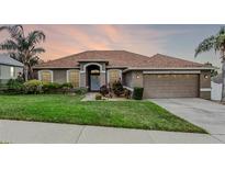 Charming single-story home featuring a well-manicured lawn, mature trees, and an attached two-car garage at 12838 Owasso Ln, Clermont, FL 34711