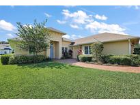 Inviting single-story home featuring lush landscaping, brick walkway, and a charming light yellow exterior at 39504 Hillrise Ln, Lady Lake, FL 32159