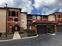 Multi-story condo building with red brick and light beige exterior, attached garages, and lush landscaping at 5560 Metrowest Blvd # 3-204, Orlando, FL 32811