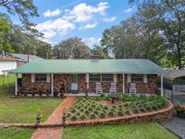 Charming brick home featuring a green metal roof, well-kept lawn and inviting front porch with rocking chairs at 10303 Se Sunset Harbor Rd, Summerfield, FL 34491