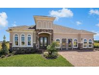 Stunning single-story home featuring stone accents, arched windows, a well-manicured lawn, and a brick driveway at 1849 Sunshine Peak Dr, Minneola, FL 34715