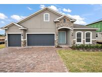 Beautiful single-Gathering home featuring a two-car garage, paver driveway, manicured lawn, and a charming stone facade at 1849 Sunshine Peak Dr, Minneola, FL 34715