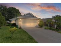 A home exterior is seen at dusk with a paved driveway leading to the garage, surrounded by mature landscaping at 2821 Mediterranean Loop, Tavares, FL 32778