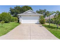 Home featuring a spacious driveway leading to an attached two-car garage and front yard with mature landscaping at 2821 Mediterranean Loop, Tavares, FL 32778