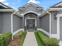 Inviting home entrance featuring a gray facade, arched doorway, and manicured landscaping at 654 Poinsett Ct, The Villages, FL 32162