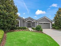 Charming gray home featuring a manicured lawn, beautiful landscaping, and an attached two-car garage at 654 Poinsett Ct, The Villages, FL 32162