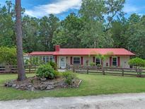 Charming single-story home featuring a red roof, shutters, landscaped front yard and a rustic wooden fence at 12288 Sw 35Th Dr, Webster, FL 33597