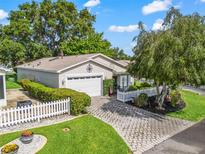 Charming home features a well-manicured lawn, stone paver driveway, and a white picket fence at 17324 Se 82Nd Pecan Ter, The Villages, FL 32162