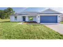 Charming single-story home featuring a blue garage door, grey roof, and nicely landscaped front yard at 472 Malauka Radl, Ocklawaha, FL 32179
