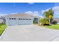 Charming home featuring a three-car garage, light-blue exterior, well-manicured lawn, and decorative driveway at 4878 Chitty Chatty Run, The Villages, FL 32163
