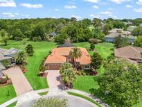 Stunning aerial view of home with lush green lawn, mature trees, circular driveway, and tiled roof at 5235 Island Terrace Ct, Lady Lake, FL 32159