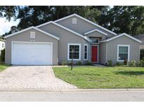 Charming single Gathering home featuring a well-manicured lawn, brick driveway, and a vibrant red front door at 5436 Astor St, Leesburg, FL 34748