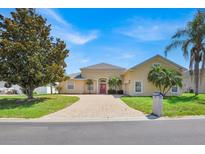 Charming, light yellow home with a brick driveway, red door, and well-maintained landscaping at 5556 Vintage View Blvd, Lakeland, FL 33812