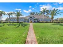 Charming single-story home featuring lush lawn, mature palms, and a welcoming brick pathway at 7350 Spring Mountain Ln, Yalaha, FL 34797