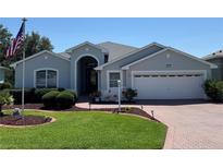 Charming single-story home featuring a well-manicured lawn and brick driveway and an American Flag at 20936 Royal St Georges Ln, Leesburg, FL 34748