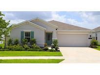 Charming single-story home features a well-manicured lawn, a two-car garage, and a decorative teal front door at 33647 Sky Blossom Cir, Leesburg, FL 34788