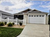 Charming single-story home featuring a well-maintained lawn, white picket fence, and an attached two-car garage at 1964 Rhett Rd, The Villages, FL 32163