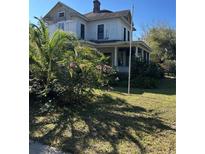 Quaint residence featuring a covered porch, mature trees and lawn at 110 S Trowell Ave, Umatilla, FL 32784