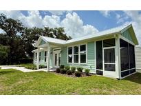 Light green house with white trim, screened in porch, and manicured landscaping at 12110 Grand Oak Ln, Oxford, FL 34484