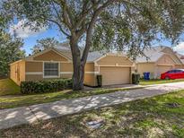 Charming single-story home featuring a tan exterior, two-car garage, mature trees, and well-maintained landscaping at 2019 Newtown Rd, Groveland, FL 34736