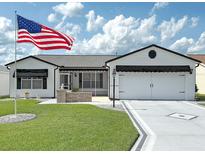 Charming single-story home with a well-manicured lawn, brick accents, and a large American flag in the front yard at 3237 Atwell Ave, The Villages, FL 32162