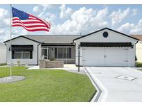 Charming one-story home with a manicured lawn, an American flag, a two-car garage, and a delightful screened in porch at 3237 Atwell Ave, The Villages, FL 32162