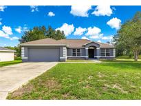 Charming single-story home featuring a two-car garage, complemented by a well-maintained front yard under a bright sky at 70 Locust Pass Run, Ocala, FL 34472