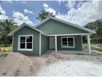 Charming green home with white trim, a cozy porch, and bright windows, set against a backdrop of blue skies and scattered clouds at 891 Cr 482C, Lake Panasoffkee, FL 33538