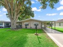 Charming single-story home featuring a covered carport, a well-manicured lawn, and mature trees providing ample shade at 1005 Richard Dr, The Villages, FL 32159