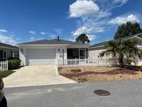 Charming single-story home with a white picket fence, a two-car garage, and a well-maintained lawn at 1199 Mathews Ln, The Villages, FL 32162