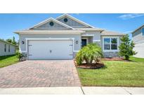 Charming single-story home with a brick driveway, two-car garage, and well-manicured lawn under a blue sky at 1696 Wilson Prairie Cir, Groveland, FL 34736