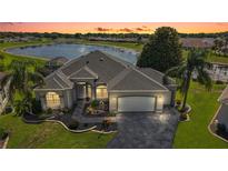 Beautifully landscaped home with a grey roof and a stunning lake view at sunset at 1920 Iglesia St, The Villages, FL 32159