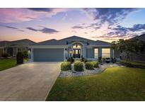 Beautiful home exterior featuring manicured landscaping, neutral paint and elegant architectural details at dusk at 3566 Gentle Ter, The Villages, FL 32163