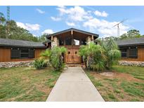 Custom home with wooden doors, stone accents, cedar siding, mature palms, and well-maintained landscaping at 672 E Belt Ave, Bushnell, FL 33513
