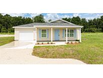Charming single-story home featuring light siding, blue shutters, a covered front porch, and an attached garage at 10128 County Road 229, Oxford, FL 34484