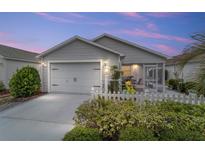Charming single-story home with light grey siding, a two-car garage, and a well-manicured front yard with a white picket fence at 2237 Jetta Way, The Villages, FL 32162