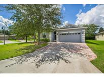 Charming single-story home with a manicured lawn, mature trees, and a brick-paved driveway leading to a two-car garage at 3604 Corsica Ln, Clermont, FL 34711