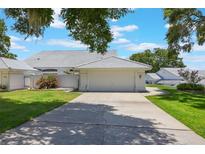 Attached two-car garage with a white door and tile roof, set within a well-maintained lawn and garden landscape at 6036 Topsail Rd, Lady Lake, FL 32159