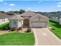 Inviting single-story home featuring a beige exterior, well-manicured lawn, and an attached two-car garage at 10927 Se 168Th Loop, Summerfield, FL 34491