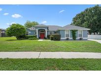 Charming single-story home featuring a red front door, well-manicured lawn, and mature landscaping at 14708 Timucua Pl, Clermont, FL 34711