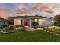 Charming single-story home featuring a red front door, well-maintained lawn, and beautiful landscaping at 16730 Se 78Th Lillywood Ct, The Villages, FL 32162