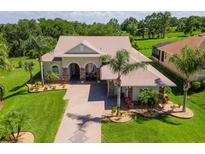 Inviting exterior of a well-manicured home featuring a brick driveway, lush lawn, and decorative palm trees at 5418 Sandy Hill Ln, Lady Lake, FL 32159