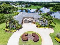 Stunning aerial view of a luxury home with a circular driveway, lush landscaping, and a serene lake backdrop at 7303 Spring Mountain Ln, Yalaha, FL 34797