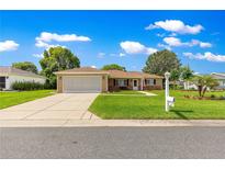 Charming single-story home with a well-manicured lawn and two-car garage, set against a backdrop of blue skies and fluffy clouds at 9790 Se 175Th St, Summerfield, FL 34491