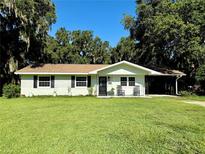 Charming single-story home featuring a well-manicured lawn, a quaint porch with rocking chairs and a convenient carport at 32511 Purdum Ave, Leesburg, FL 34788