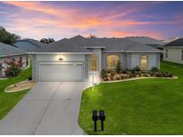 Charming home showcasing manicured landscaping and an attached two-car garage, bathed in warm sunset hues at 16863 Se 110Th Court Rd, Summerfield, FL 34491