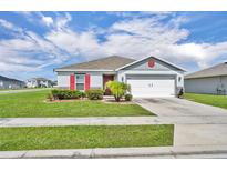 Charming single-Gathering home featuring a two-car garage, red accents, manicured lawn, and well-maintained landscaping at 2488 Begonia St, Mascotte, FL 34753