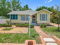 Charming yellow home with blue shutters, complemented by a brick walkway and lush landscaping at 1109 Edmonds St, Leesburg, FL 34748